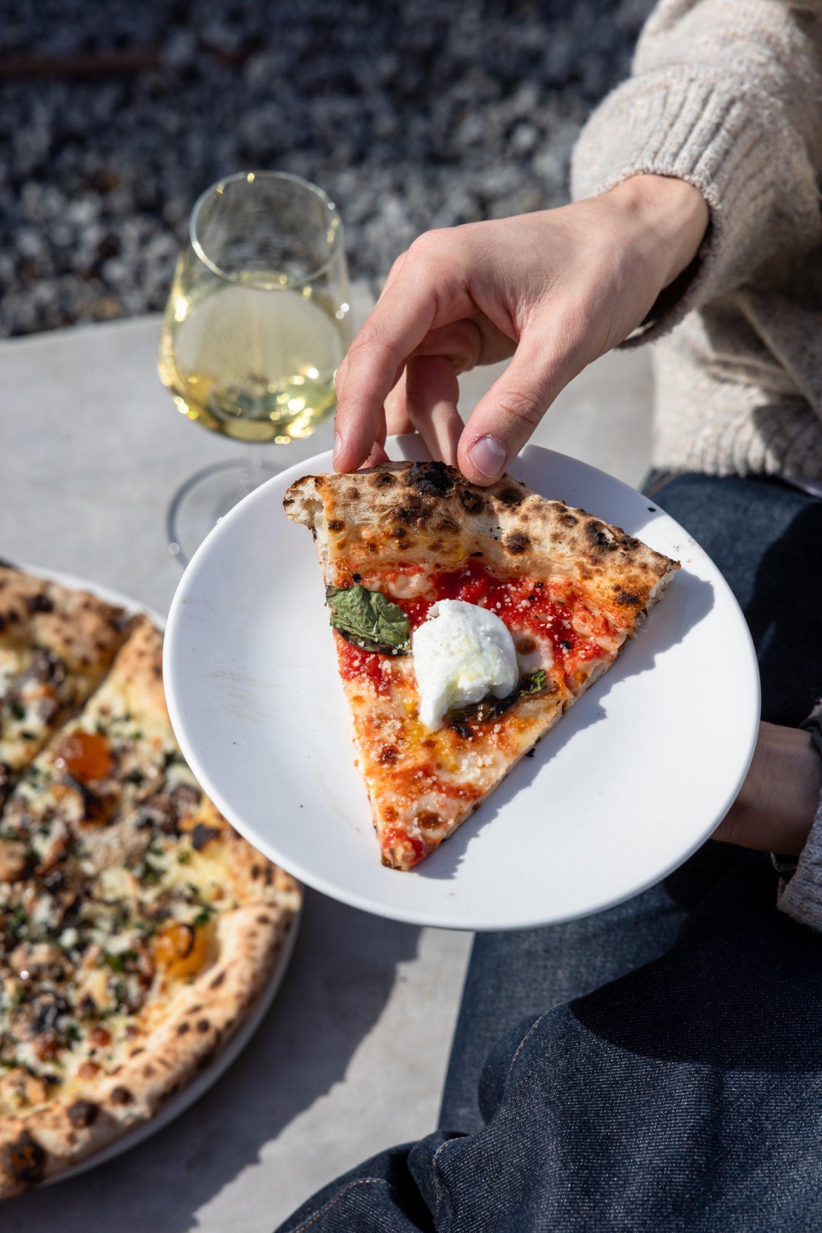 Lifting a slice of pizza at a sunny table at The Observatory