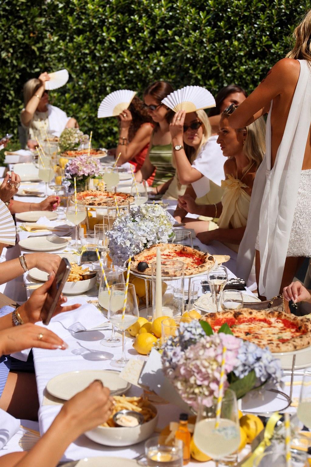 Guests at a long-table hens lunch with pizza, lemons and hydrangeas in The Observatory courtyard